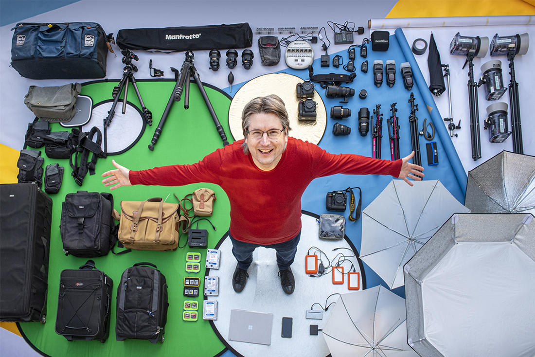 Award-winning photographer Jonathan Banks standing with arms stretched with his camera equipment laid out on the floor.